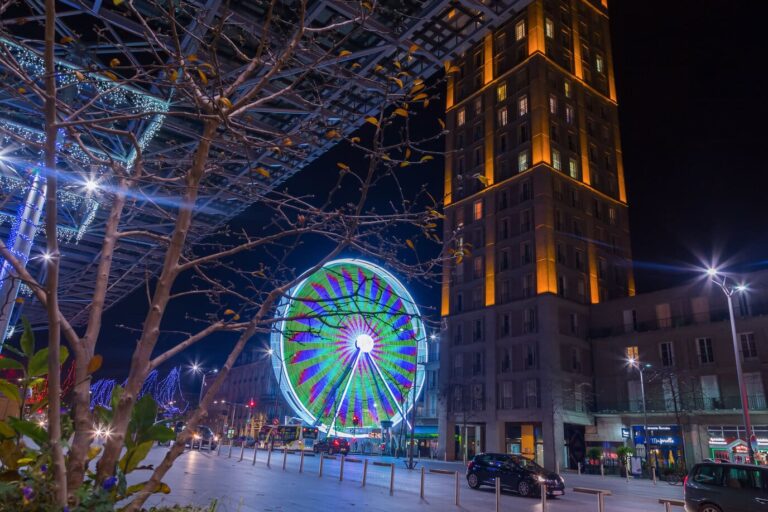 Grande roue illuminée en vert et violet au pied de la tour Perret éclairée, de nuit