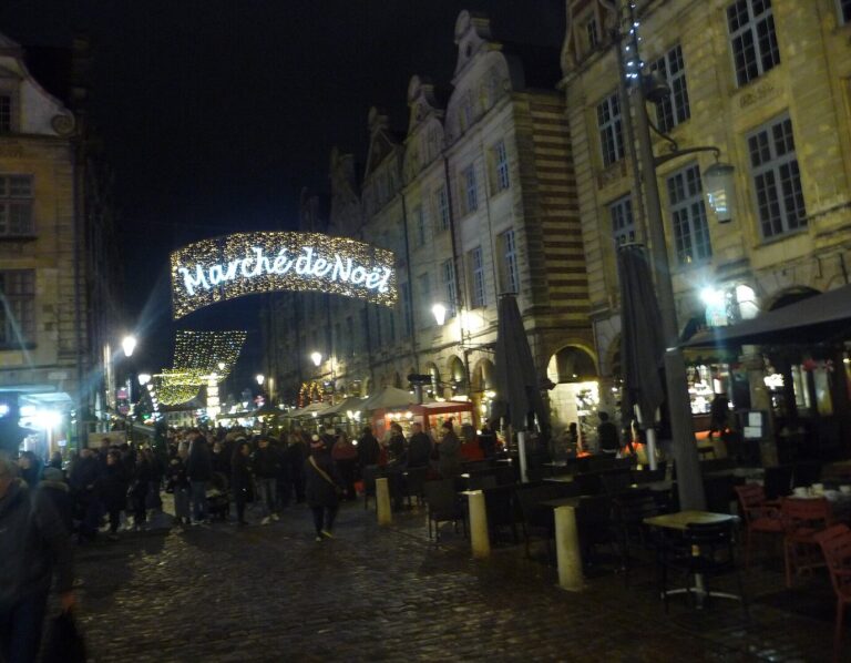 Une rue animée d’Arras sous une arche lumineuse « Marché de Noël », de nuit