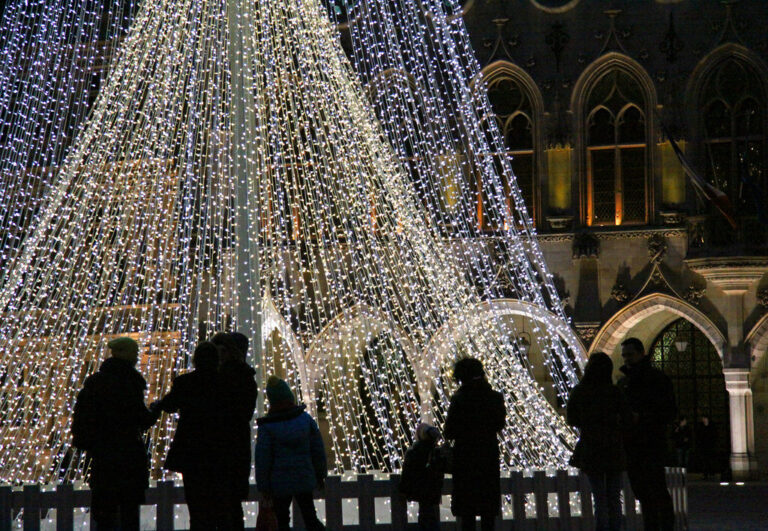 Silhouettes de promeneurs au pied d’un sapin de lumières blanches, devant l’hôtel de ville d’Arras