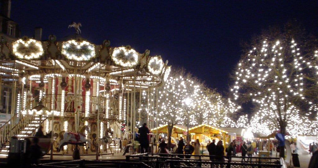 Carrousel illuminé et arbres couverts de guirlandes blanches entre les chalets du marché de Noël de Bordeaux, de nuit