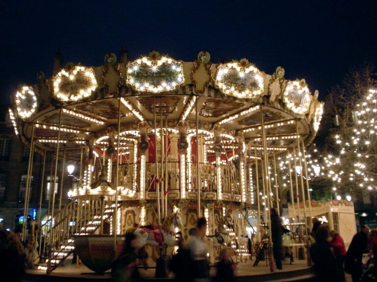 Carrousel à deux étages couronné de guirlandes lumineuses, avec les arbres illuminés du marché en arrière-plan