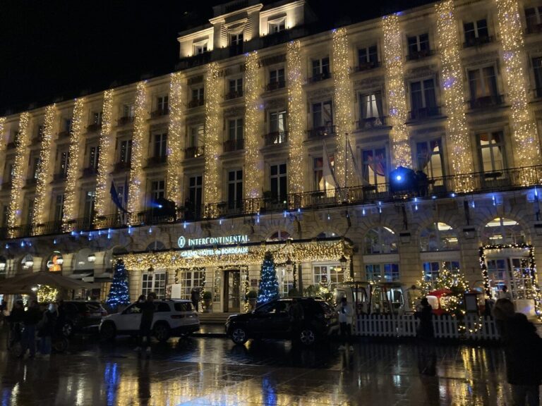 La façade du Grand Hôtel de Bordeaux tendue de rideaux de lumière et ses sapins décorés, de nuit