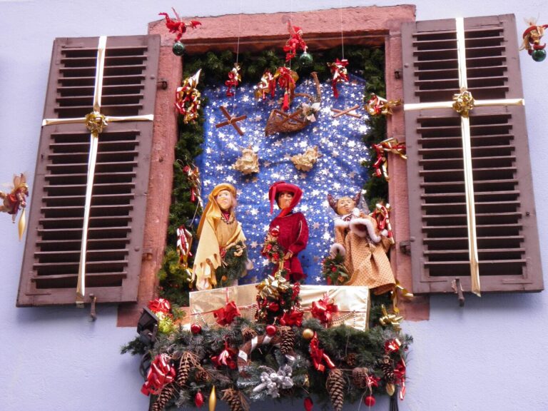 Une fenêtre aux volets ouverts décorée d’une crèche, de branches de sapin et de nœuds rouges