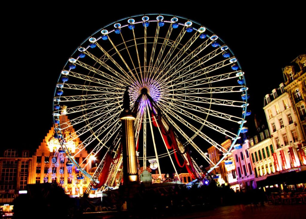 La grande roue illuminée sur la Grand-Place de Lille, derrière la colonne de la Déesse, entre les façades éclairées
