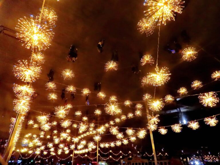 Des étoiles et guirlandes lumineuses dorées suspendues au-dessus du Vieux-Port, vues d’en dessous dans la nuit