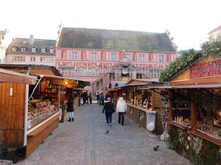 Allée de chalets en bois menant à l’ancien hôtel de ville rose de la place de la Réunion, en journée