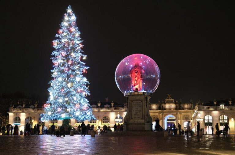 La statue de Stanislas placée dans une bulle lumineuse rose à côté du sapin illuminé, place Stanislas de nuit