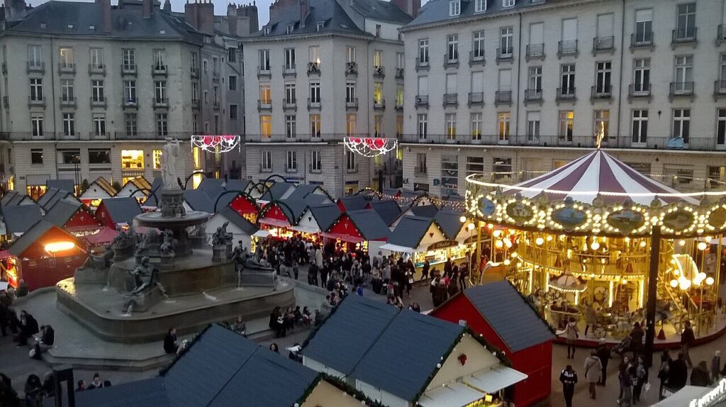 La place Royale de Nantes au crépuscule, avec les chalets du marché de Noël, le carrousel illuminé et la fontaine