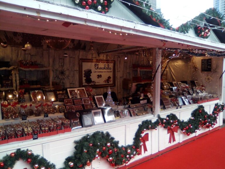 Étal d’un chalet blanc décoré de guirlandes de sapin et de nœuds rouges au marché de Noël de La Défense