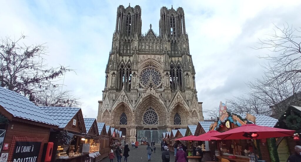 Chalets du marché de Noël aux toits enneigés sur la place du Cardinal-Luçon, face à la façade de la cathédrale Notre-Dame de Reims