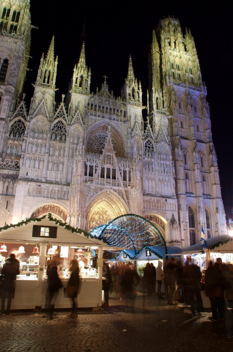 La façade gothique de la cathédrale Notre-Dame de Rouen éclairée de nuit, au-dessus des chalets du marché de Noël