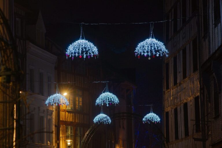 Suspensions lumineuses en forme de boules givrées au-dessus de la rue Eau-de-Robec et de ses maisons à pans de bois, la nuit