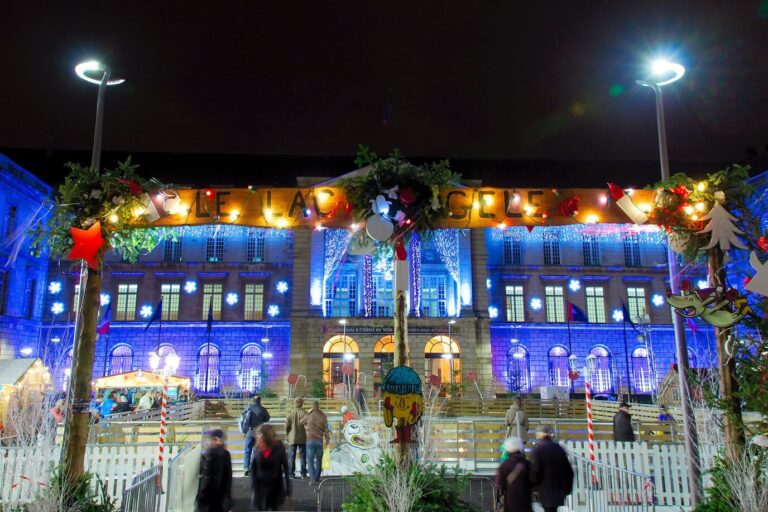 Patinoire décorée de sapins et de guirlandes devant la façade illuminée en bleu de l’hôtel de ville de Rouen