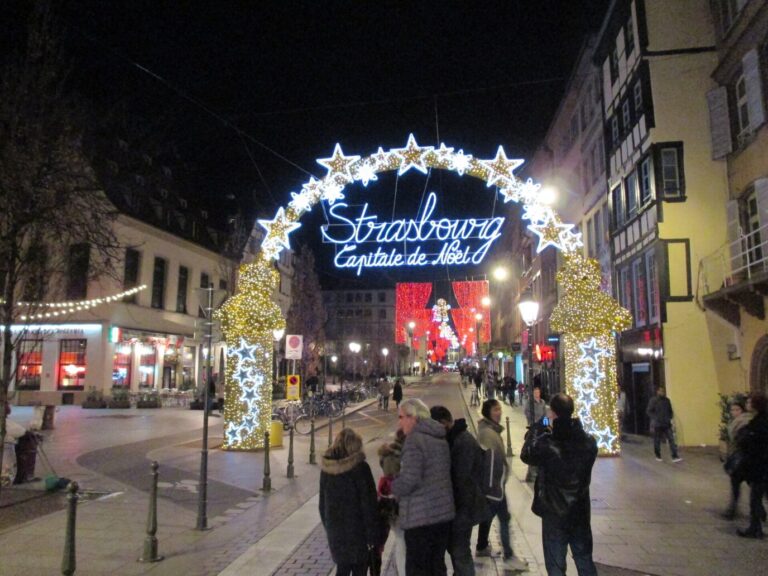 L’arche lumineuse « Strasbourg capitale de Noël » au-dessus d’une rue du centre, avec des promeneurs, la nuit