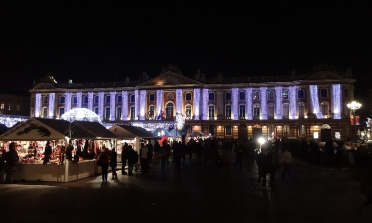 Le marché de Noël de la place du Capitole de nuit, chalets éclairés au premier plan devant la façade illuminée du Capitole