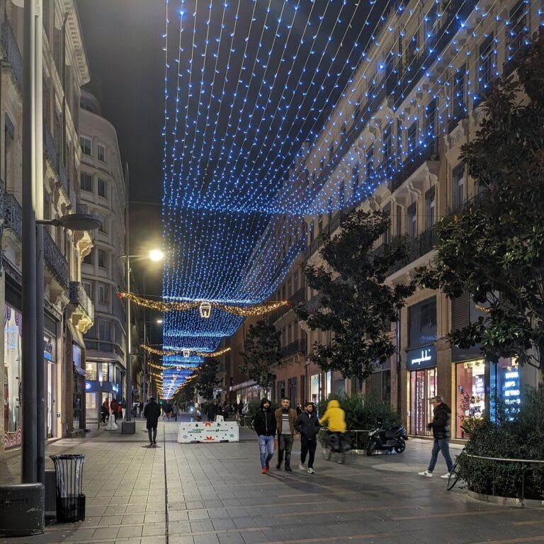 La rue d’Alsace-Lorraine couverte d’un ciel de guirlandes lumineuses, avec des passants le soir