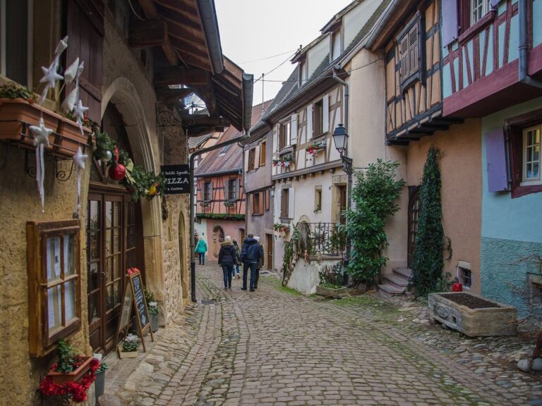 Ruelle pavée d’Eguisheim bordée de maisons colorées, étoiles de Noël accrochées aux jardinières