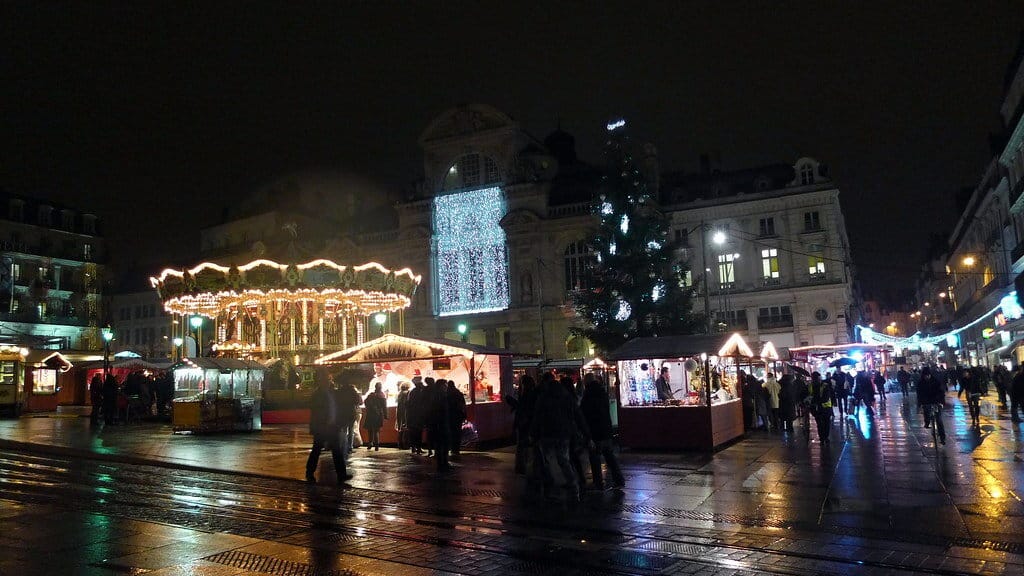 La place du Ralliement de nuit après la pluie, avec le carrousel illuminé, les chalets du marché, le grand sapin et la façade éclairée du Grand Théâtre
