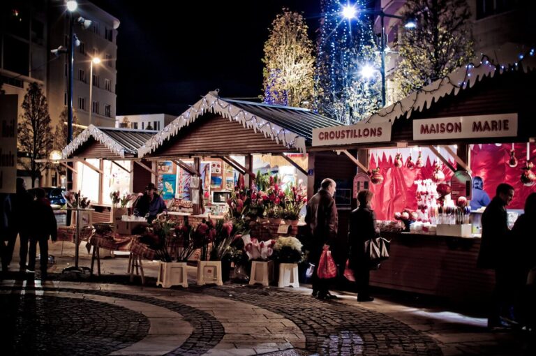 Chalets en bois du marché de Noël de Caen, étals de fleurs et de friandises, sous des arbres illuminés