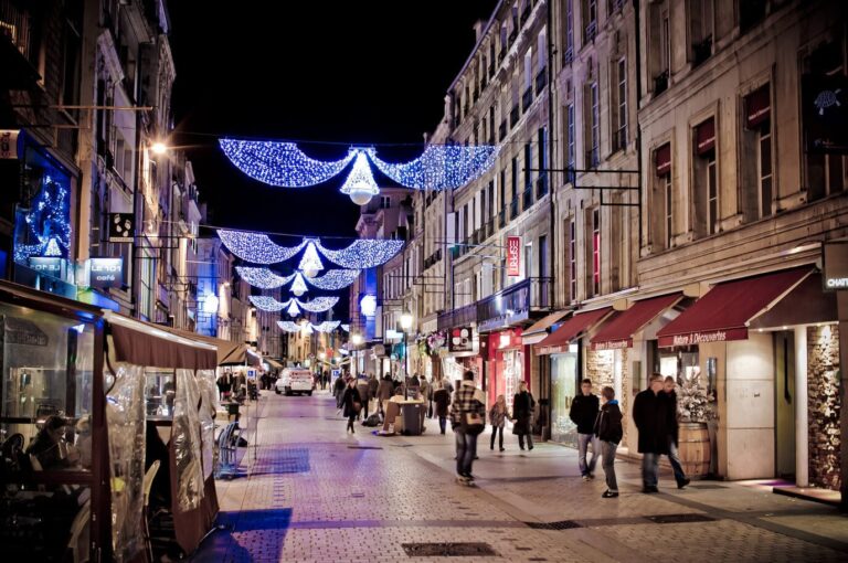 Guirlandes lumineuses bleues et blanches au-dessus d’une rue piétonne commerçante du centre de Caen, le soir