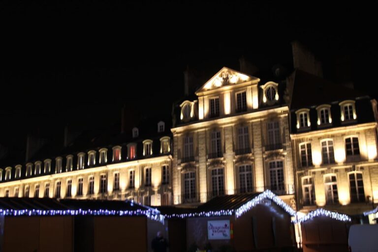 Toits de chalets bordés de guirlandes devant des façades classiques éclairées, de nuit