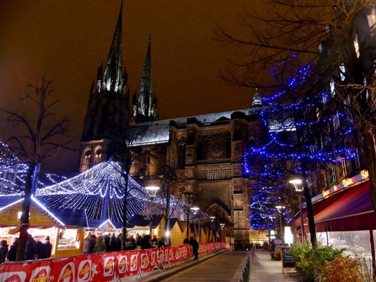 Les chalets illuminés du marché de Noël au pied de la cathédrale Notre-Dame-de-l’Assomption et de ses flèches de pierre noire, la nuit