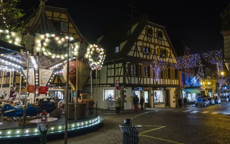 Manège ancien illuminé devant des maisons à colombages et des guirlandes, place de l’Étoile