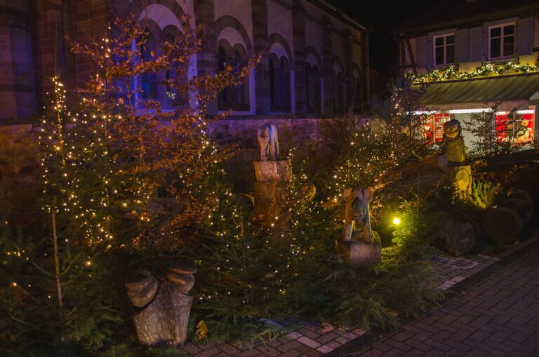 Sapins couverts de guirlandes et figurines sculptées dans le bois, décor de Noël nocturne dans le centre d’Obernai