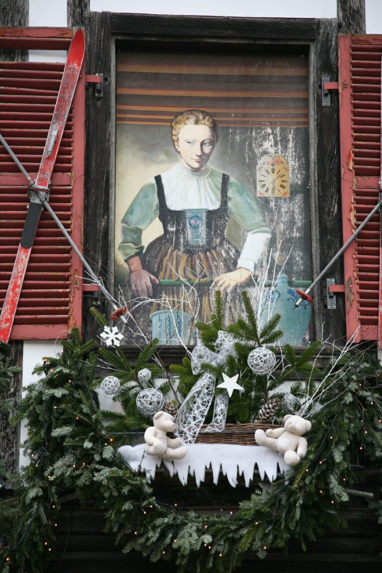 Fenêtre de maison alsacienne peinte d’une figure en costume traditionnel et ornée d’une couronne de sapin et de décorations blanches
