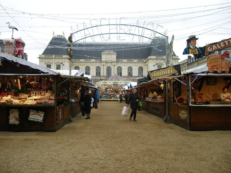 Allée de chalets en bois sous l’arche du marché de Noël, face à la façade du Parlement de Bretagne
