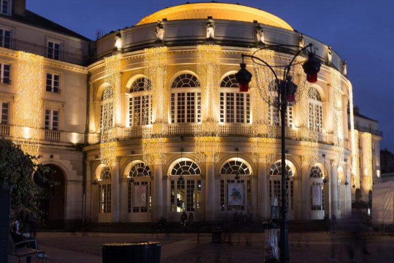 La façade arrondie de l’opéra de Rennes parée de guirlandes lumineuses, au crépuscule