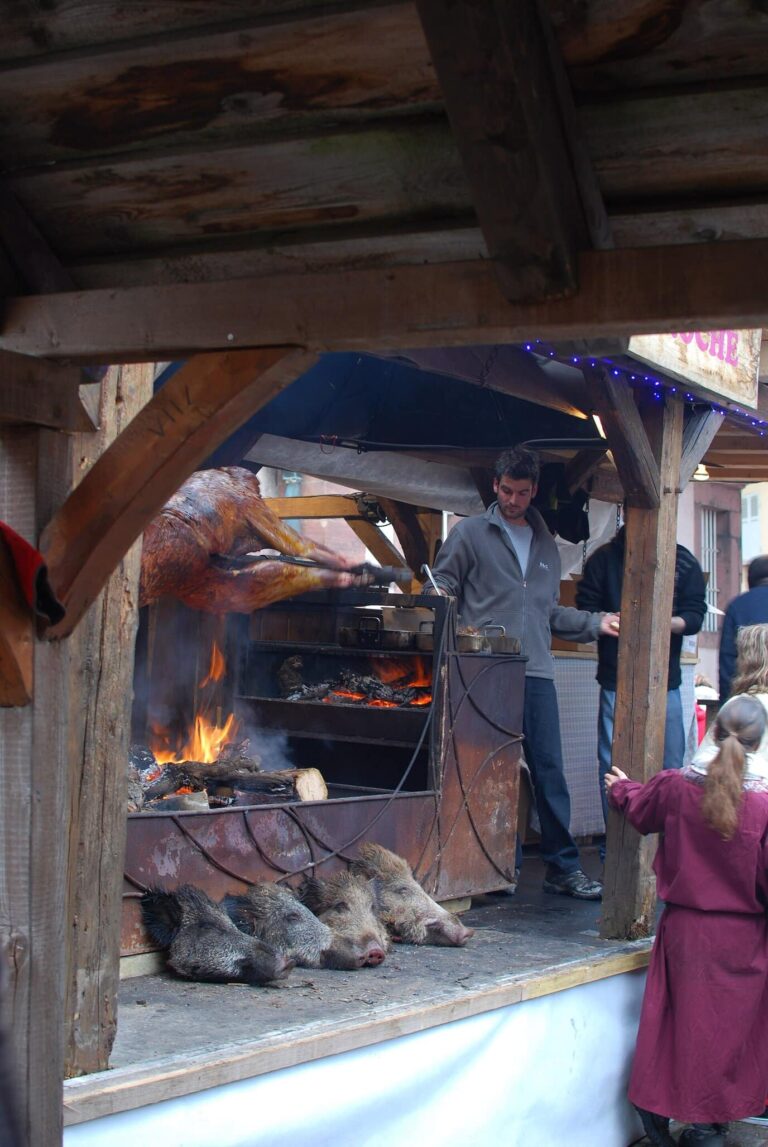 Rôtissoire sous un auvent en bois du marché de Noël médiéval, viandes à la broche au-dessus du feu