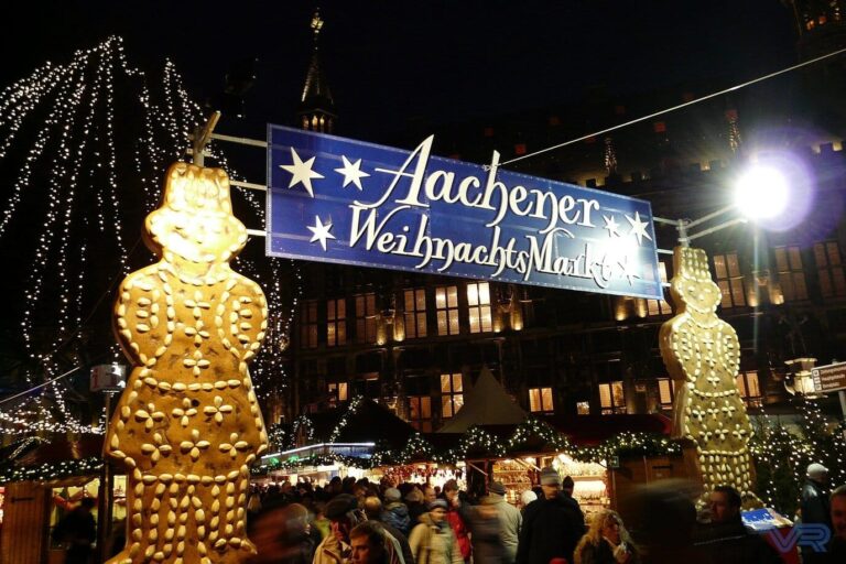 Deux grands bonshommes en pain d’épices illuminés encadrant la banderole « Aachener Weihnachtsmarkt », la nuit