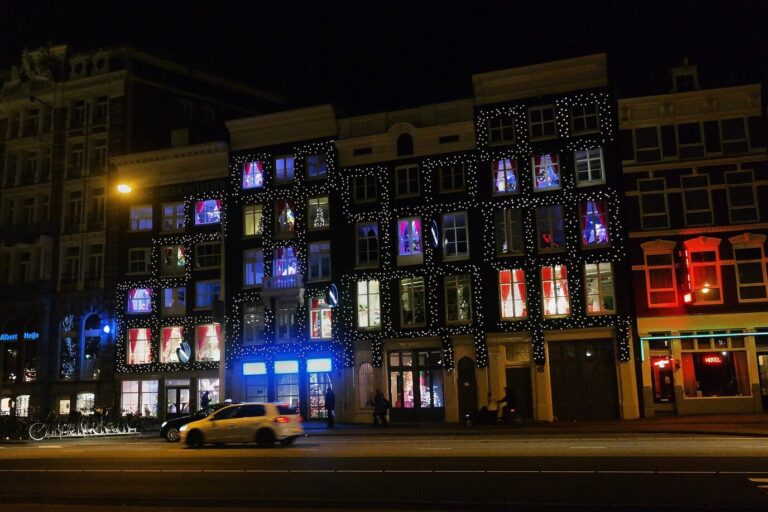 Façades du Prins Hendrikkade couvertes de guirlandes lumineuses, la nuit, face à la gare centrale d’Amsterdam
