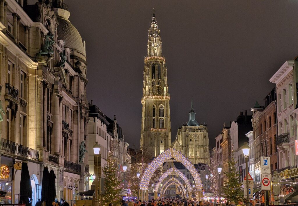 La rue Suikerrui illuminée la nuit, avec une arche lumineuse et des sapins, menant à la tour éclairée de la cathédrale Notre-Dame d’Anvers