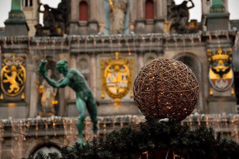 La statue de la fontaine de Brabo devant une grosse boule de Noël tressée, sur fond de façade de l’hôtel de ville décorée
