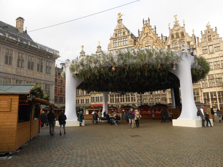 Chalets en bois et grande rotonde végétale décorée pour Noël, devant les maisons de guildes à pignons du centre d’Anvers