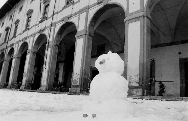 Un bonhomme de neige devant les arcades de la Loggia de Vasari, sur la piazza Grande enneigée, en noir et blanc