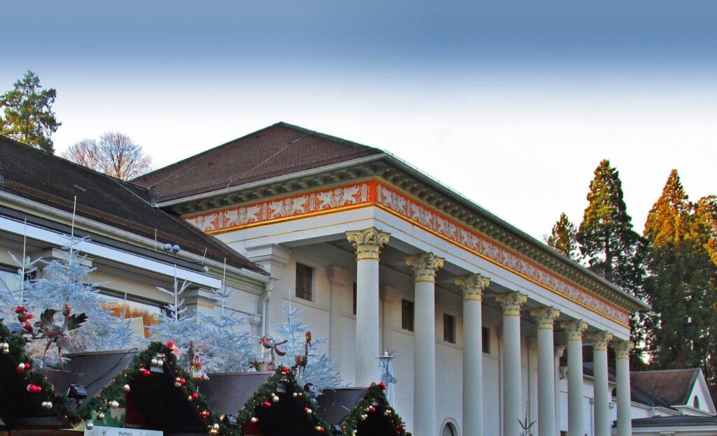 La colonnade néoclassique du Kurhaus de Baden-Baden derrière les toits des chalets du marché de Noël, décorés de guirlandes et de sapins blancs