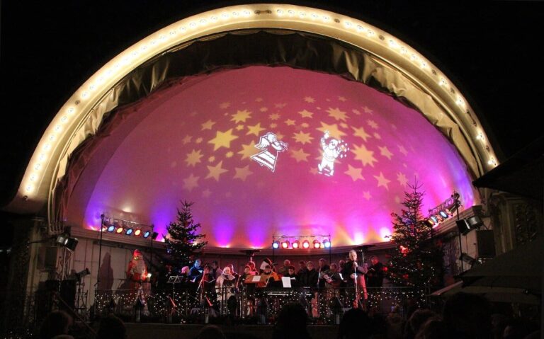 Concert sous la conque illuminée du Kurgarten, éclairée en rose et parsemée d’étoiles projetées, entre deux sapins, la nuit