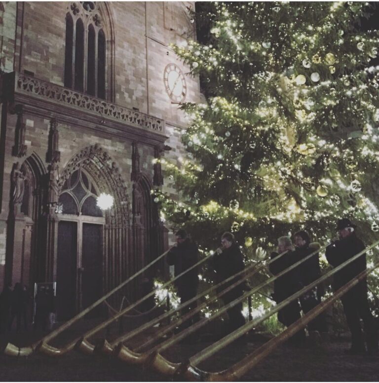 Joueurs de cor des Alpes devant le portail de la cathédrale de Bâle, à côté du sapin illuminé du Münsterplatz
