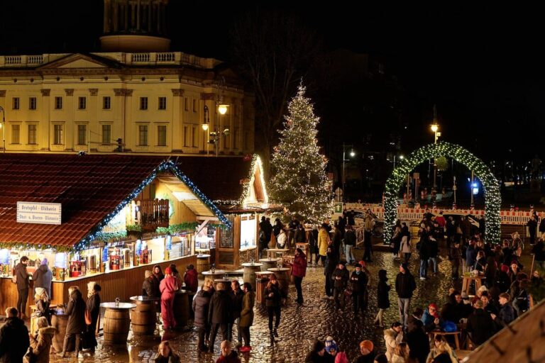 Des chalets décorés de guirlandes et un grand sapin illuminé devant une aile du château de Charlottenburg, avec une arche lumineuse au fond