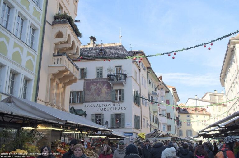 La piazza delle Erbe de Bolzano sous des guirlandes de sapin, avec la façade peinte de la Casa del Torchio et les étals du marché