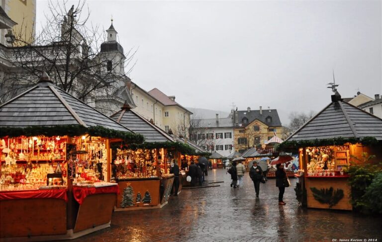Chalets illuminés du marché de Noël alignés sur le pavé mouillé de la piazza Duomo, la cathédrale à gauche