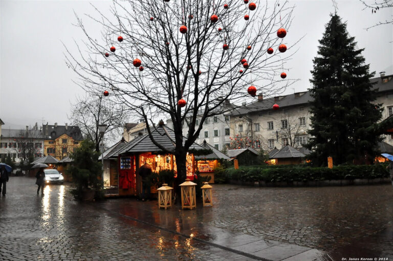 Grand sapin, arbre garni de boules rouges et chalets éclairés du marché de Noël de Bressanone, par temps gris