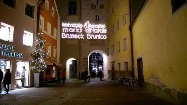 Enseigne lumineuse « Weihnachtsmarkt Bruneck, Mercatino di Natale Brunico » au-dessus d’une porte de la vieille ville, à la nuit tombée