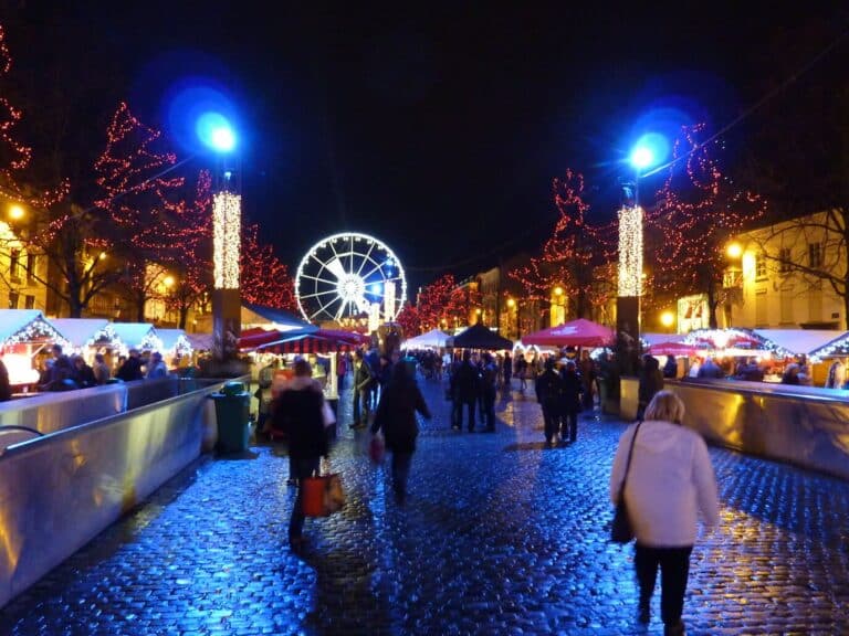 Une allée de chalets du marché aux Poissons sous les arbres illuminés, avec la grande roue au fond, la nuit