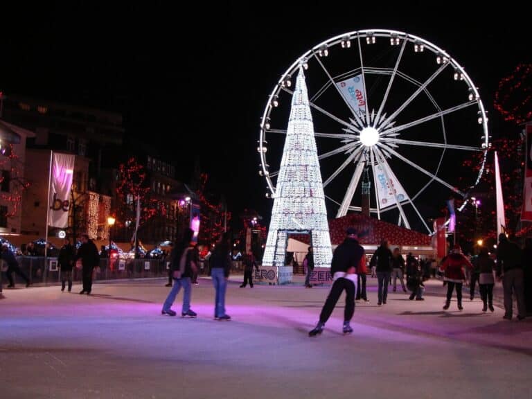 Des patineurs sur la patinoire à ciel ouvert, devant un sapin lumineux et la grande roue éclairée