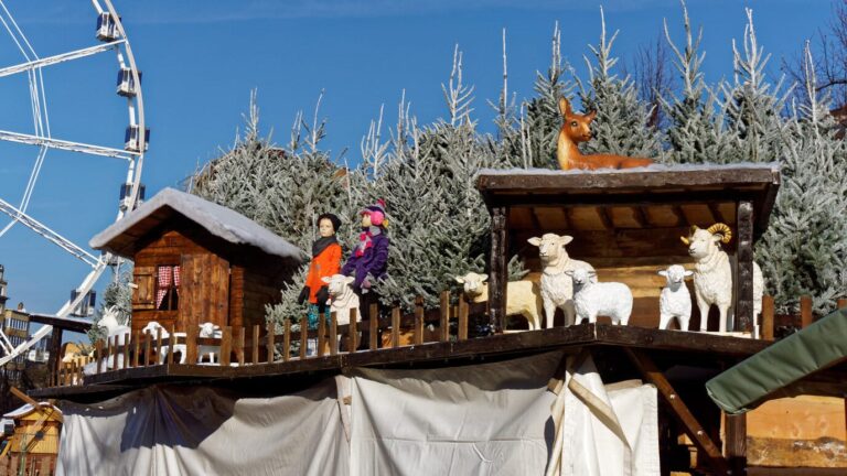 Un décor de crèche et de moutons sur le toit d’un chalet, devant des sapins givrés et la grande roue