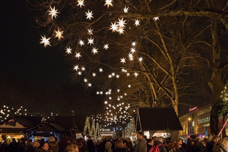 Des étoiles lumineuses suspendues dans les arbres au-dessus des chalets du marché des anges, sur le Neumarkt, la nuit